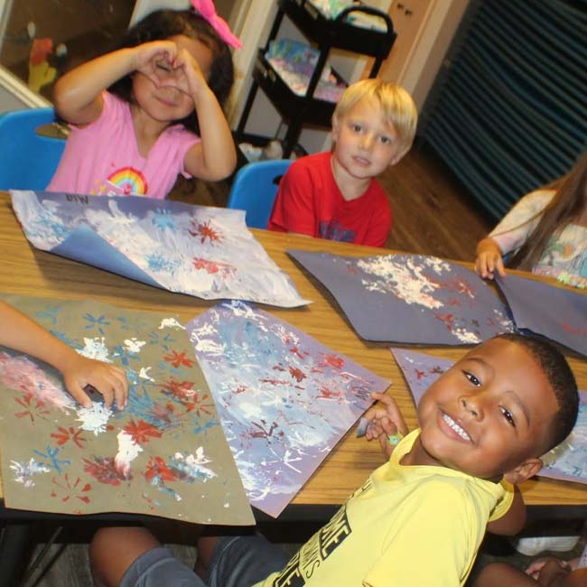 Preschoolers at Lean Valley Daycare smile, holding and making colorful abstract art pieces.
