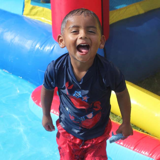Smiling child from KidCare Learning Center stands in a shallow pool near an inflatable slide.