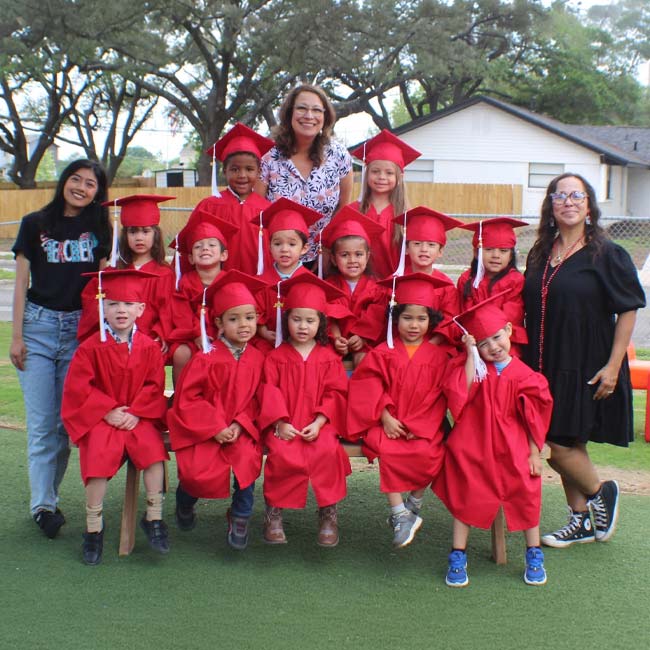 Young children in red gowns with KidCare Learning Center staff, all smiling outdoors.