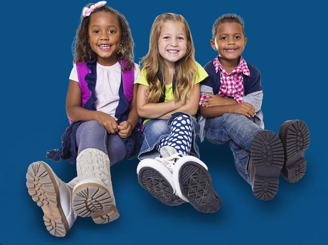 Three smiling toddlers sit on the floor, showing joy at Lean Valley Daycare's warm environment.