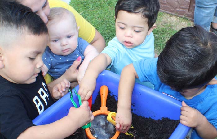 Preschoolers and toddlers at KidCare Learning Center explore soil outdoors with colorful tools.